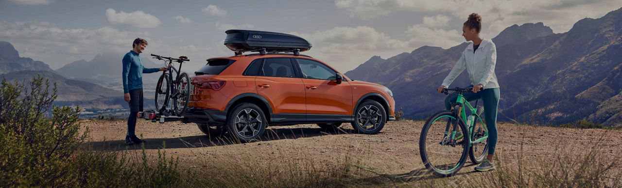 An orange Audi vehicle parked on a hillside with a man dismounting a bike form the vehicle